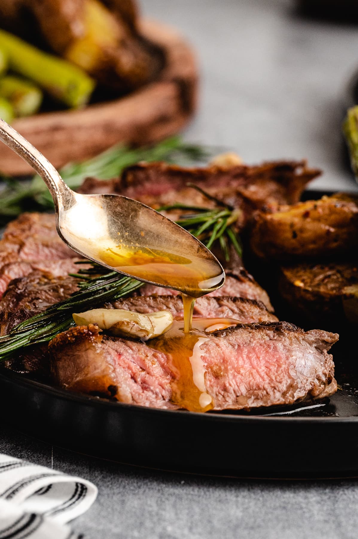 A spoon drizzling butter over perfect steak on a plate
