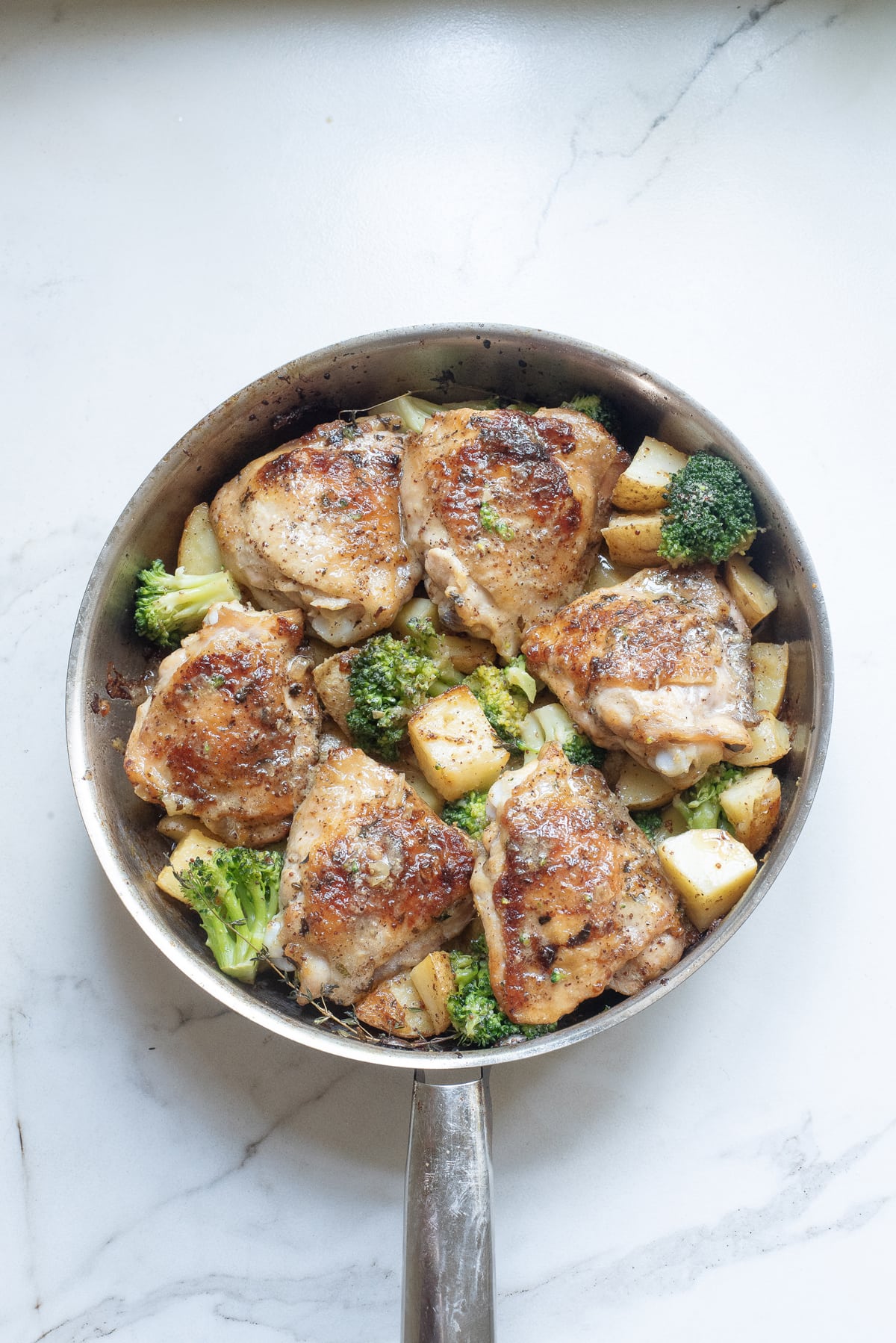 Cooked chicken thighs, potatoes, and broccoli in a metal skillet