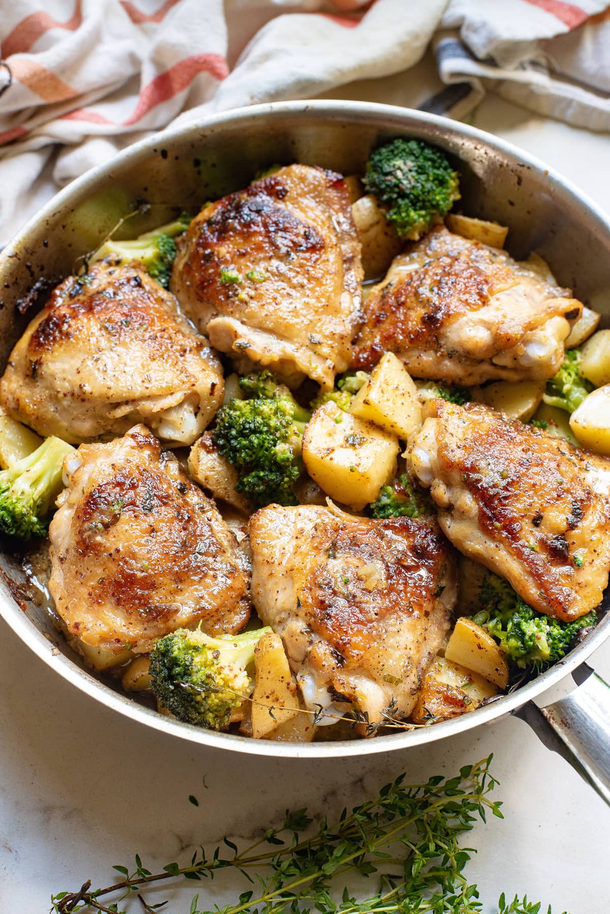 Angled view of a skillet of honey mustard chicken and potatoes with broccoli
