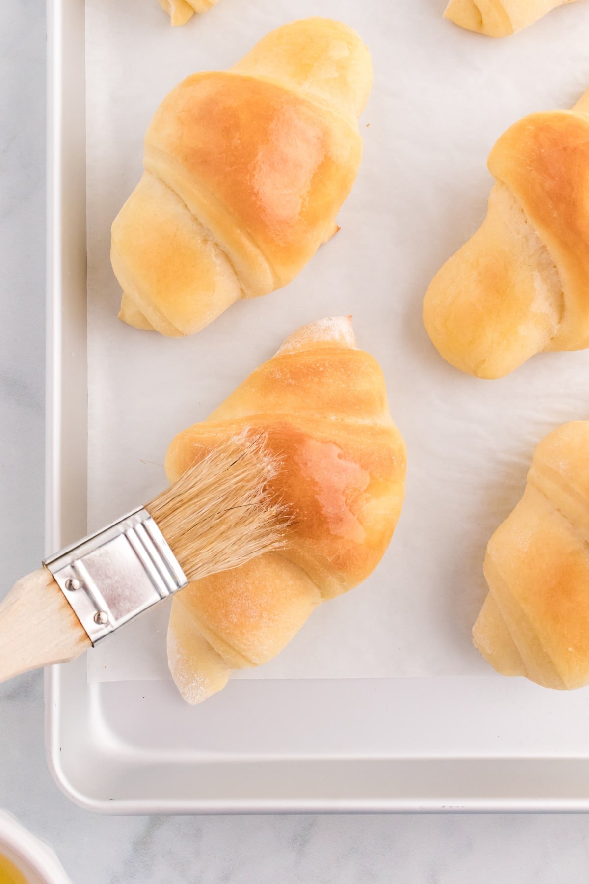 Butter being brushed on freshly baked crescent rolls