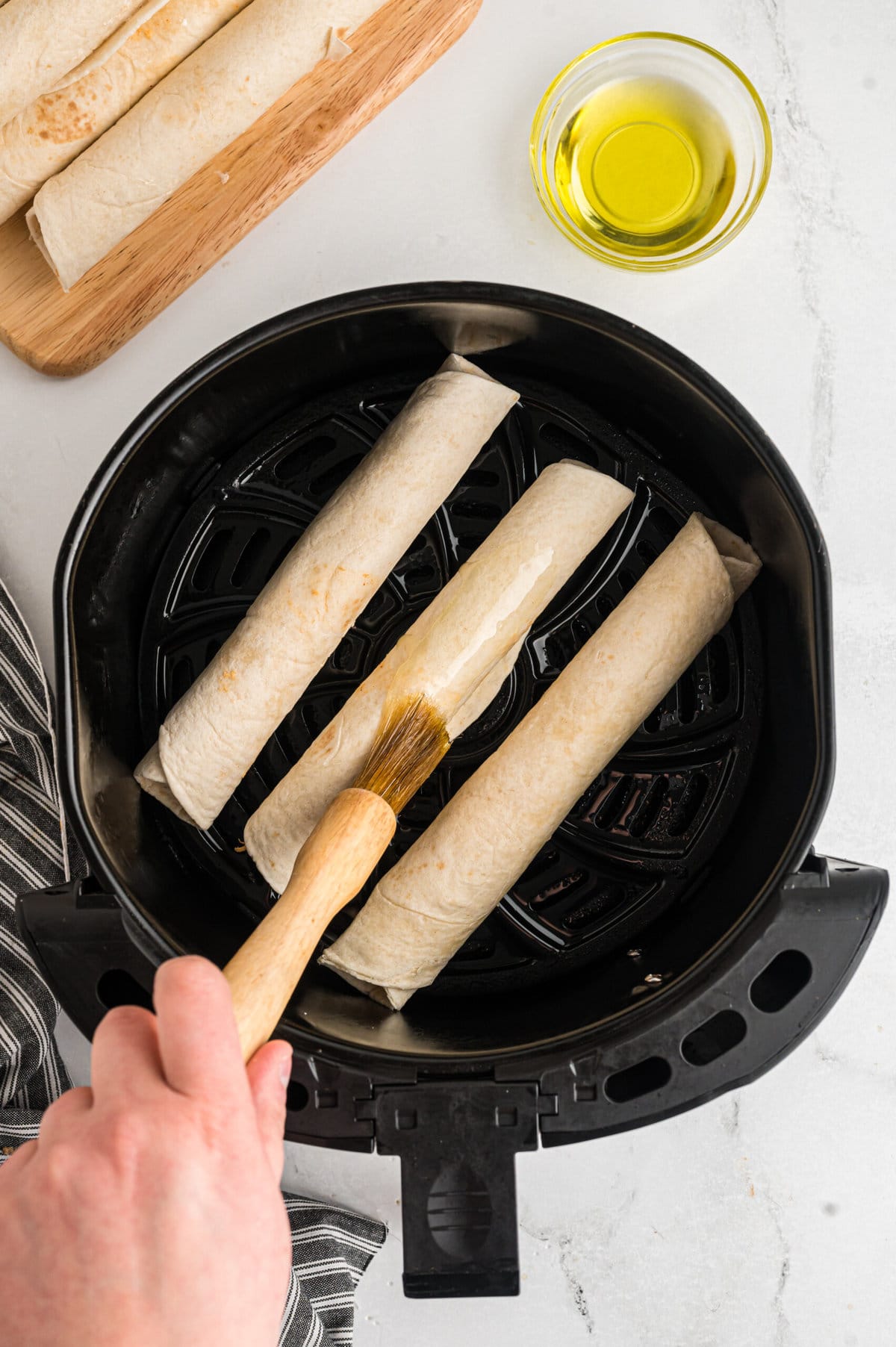 Air Fryer Chicken Taquitos being brushed with oil.