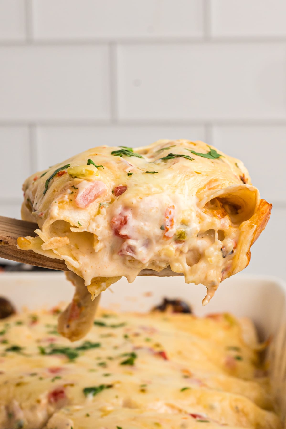 A wooden spoon lifting white queso enchiladas from the baking dish