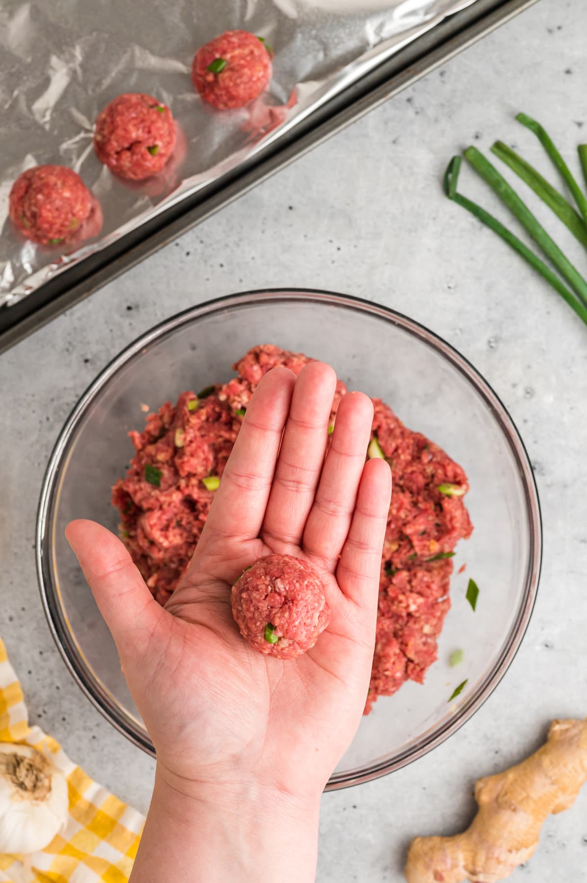A hand holding a raw beef meatball