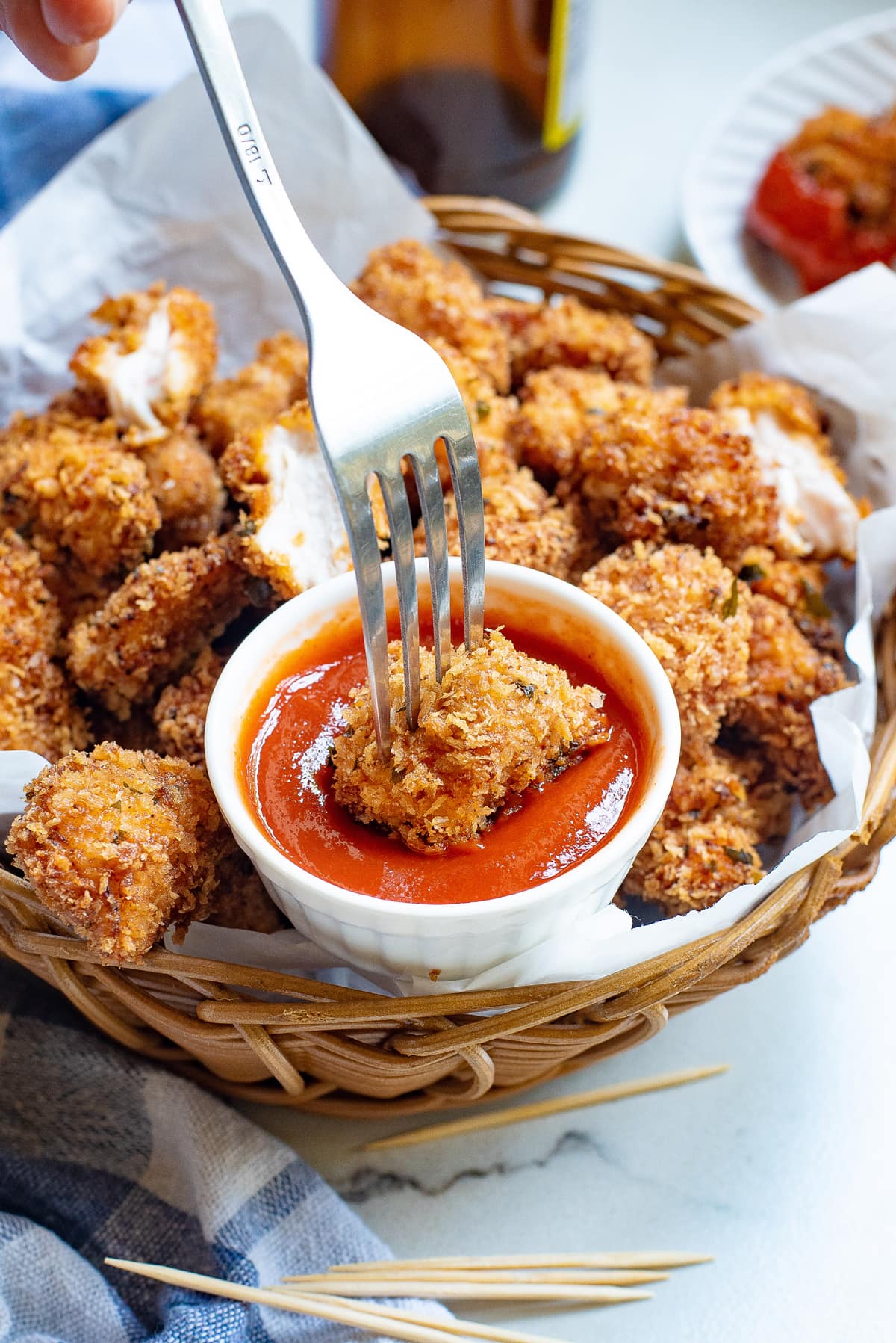 A fork dunking a piece of popcorn chicken in ketchup
