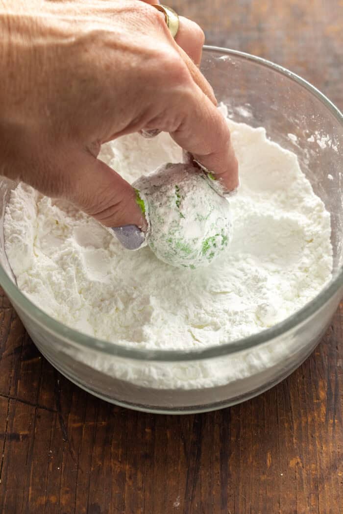A hand rolling balls of cookie dough in powdered sugar