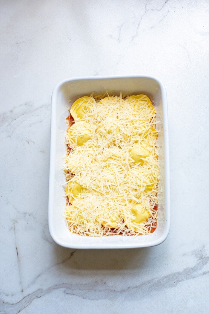 cheese on top of ravioli and sauce for baked ravioli in white rectangle baking dish