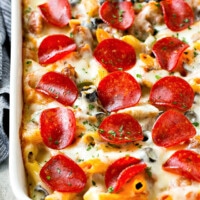 pizza pasta bake in white baking dish with pepperoni and cheese on top and blue napkin