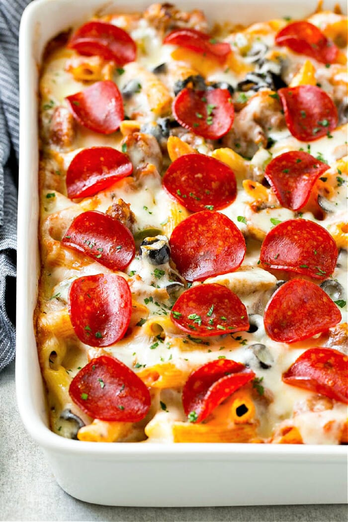 pizza pasta bake in white baking dish with pepperoni and cheese on top and blue napkin