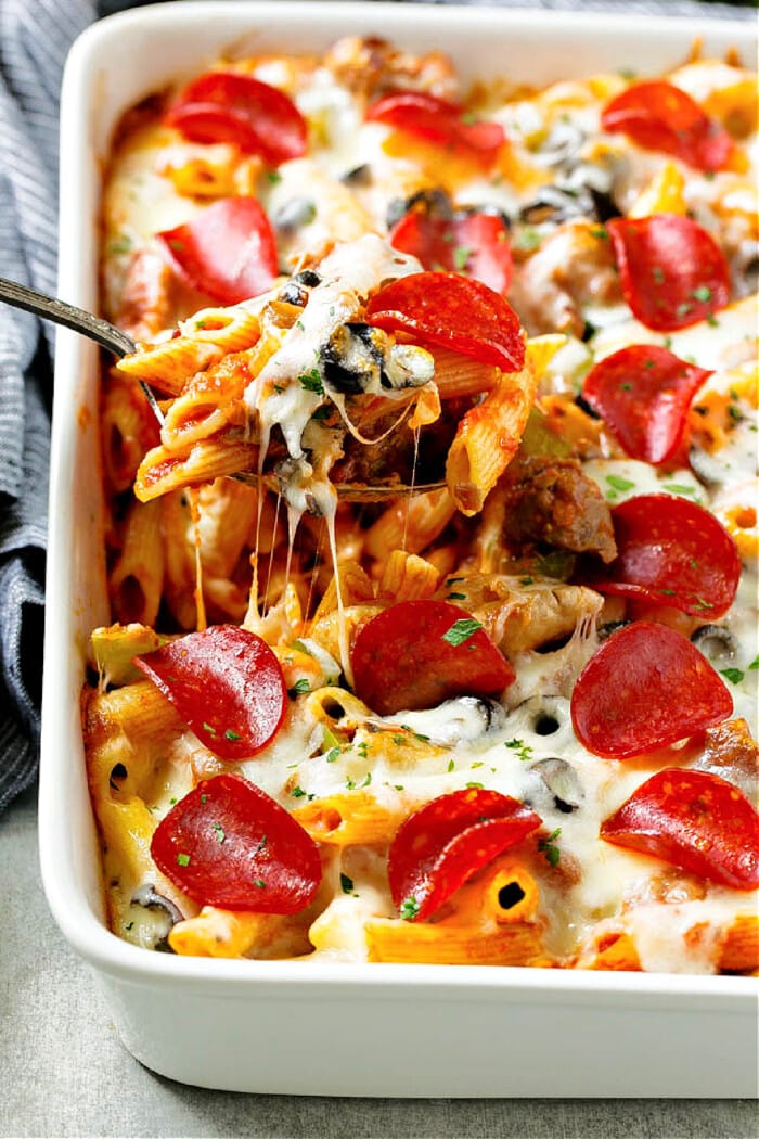 pizza pasta bake in white baking dish with pepperoni and cheese on top and blue napkin and spoon serving