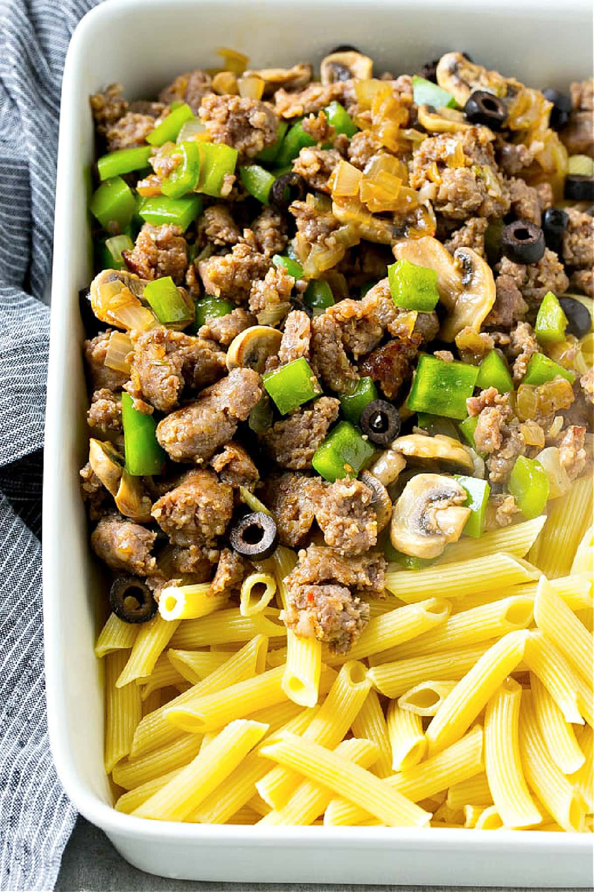 pasta cooked in white baking dish with sausage, mushrooms, peppers, onions, olives