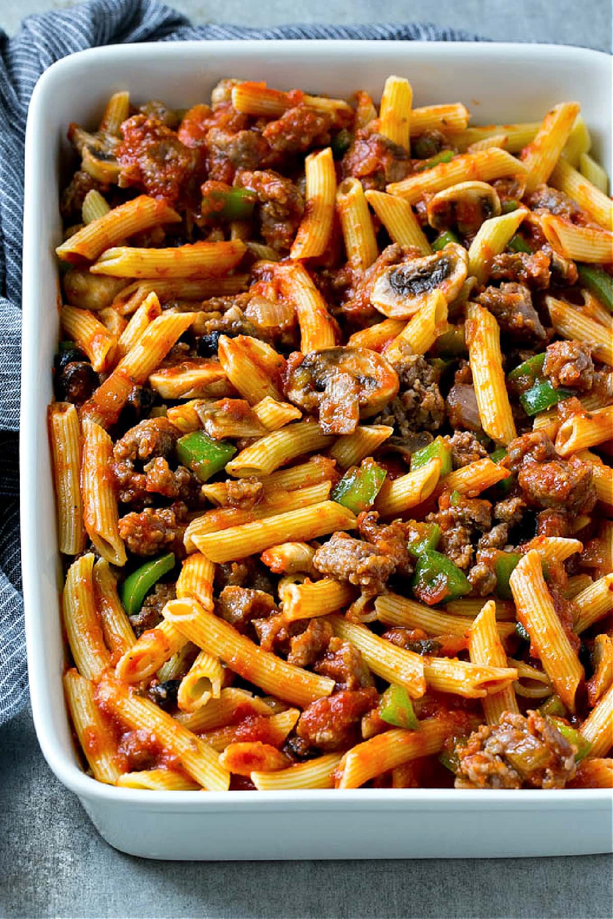 pasta cooked in white baking dish mixed with sausage, mushrooms, peppers, onions, olives and red sauce