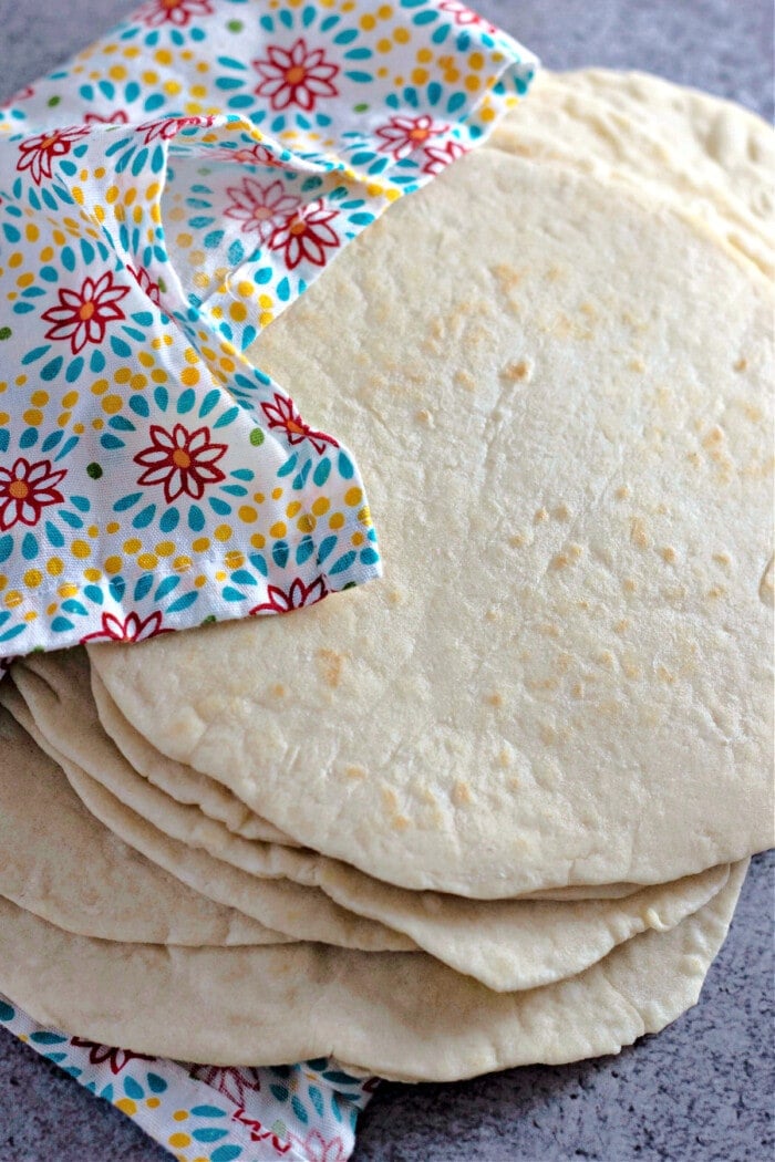 homemade flour tortillas stacked with bright colored napkin on gray board