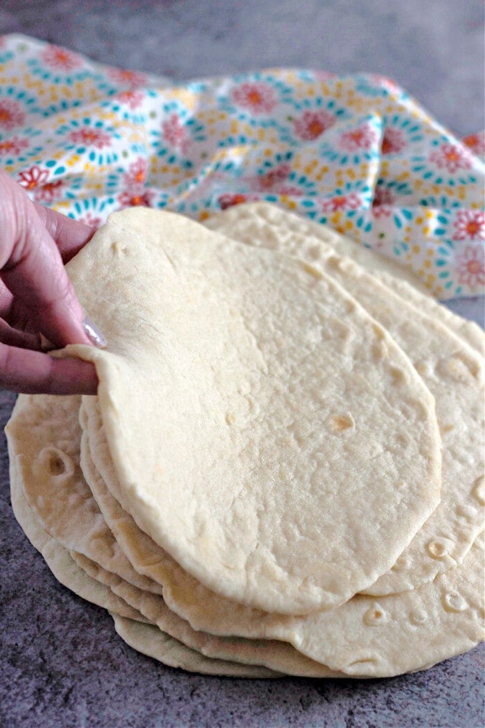 hand holding homemade flour tortillas stacked with bright colored napkin