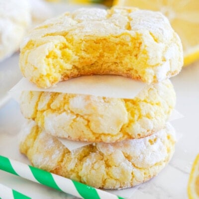 lemon crinkle cookies stacked with bite out with lemons and green striped straws