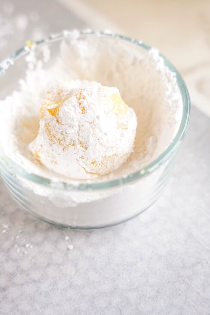 cookie dough coated in powdered sugar in clear glass bowl