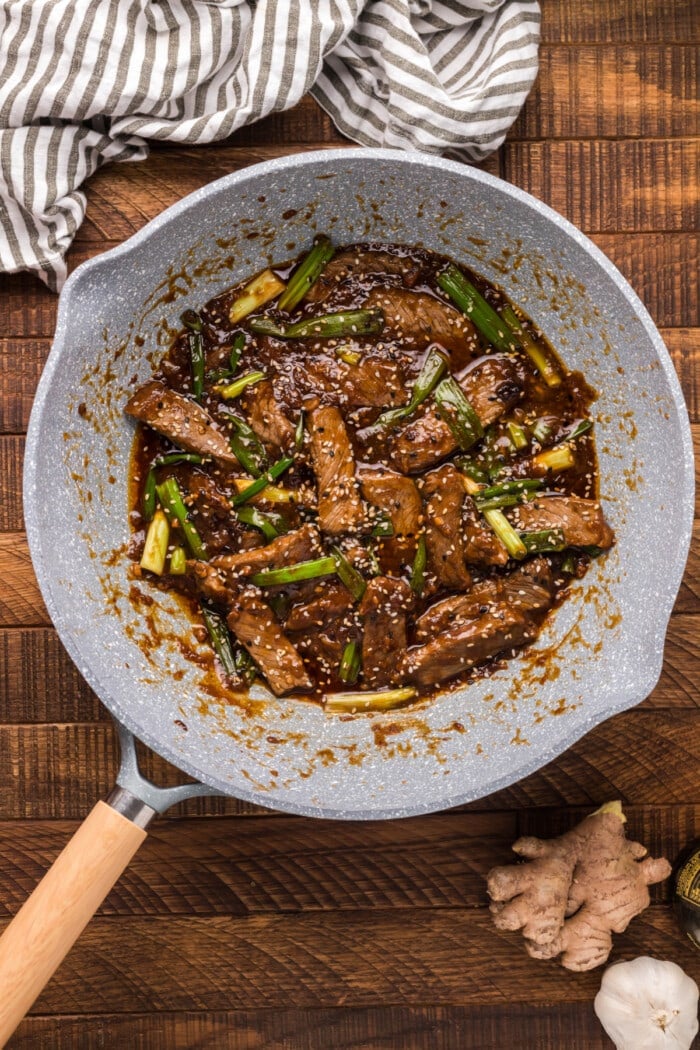 green onions and sesame seeds with beef in gray wok pan