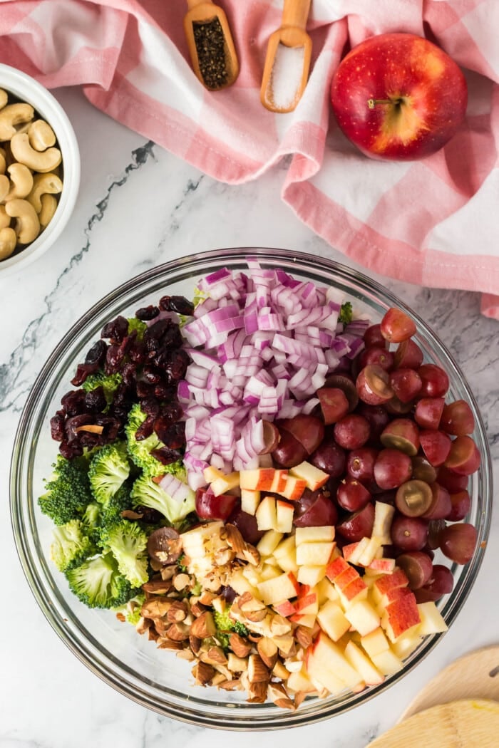 Broccoli, onions, grapes, apples, and craisins in a bowl.