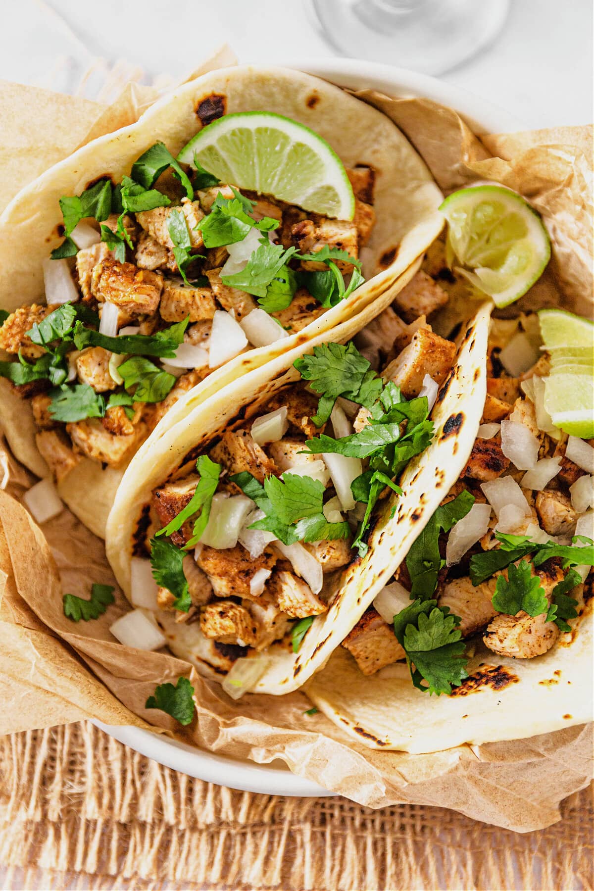 bowl with chicken tacos topped with onion, cilantro and lime wedges