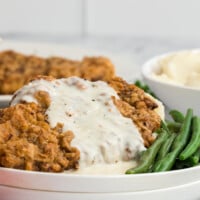 Chicken fried steak with gravy on a plate with green beans