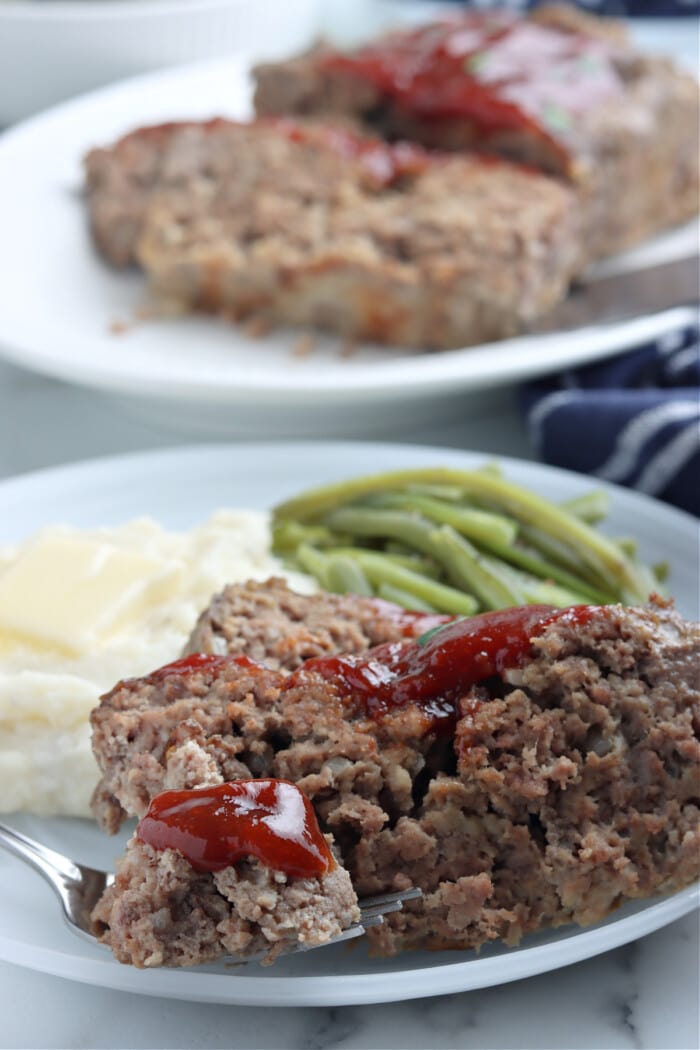 meatloaf with glaze on white plate with mashed potatoes and green beans
