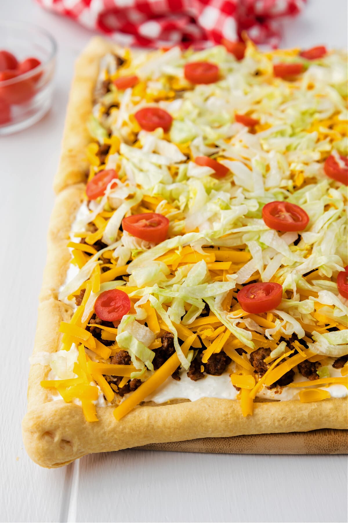 taco pizza with lettuce, tomatoes and cheese on cutting board