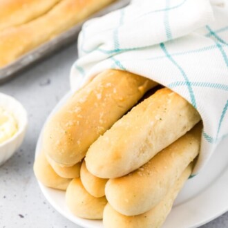 Homemade breadsticks wrapped in a towel on a plate