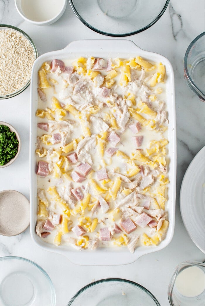 cheese sauce with pasta, chicken and ham in white casserole dish