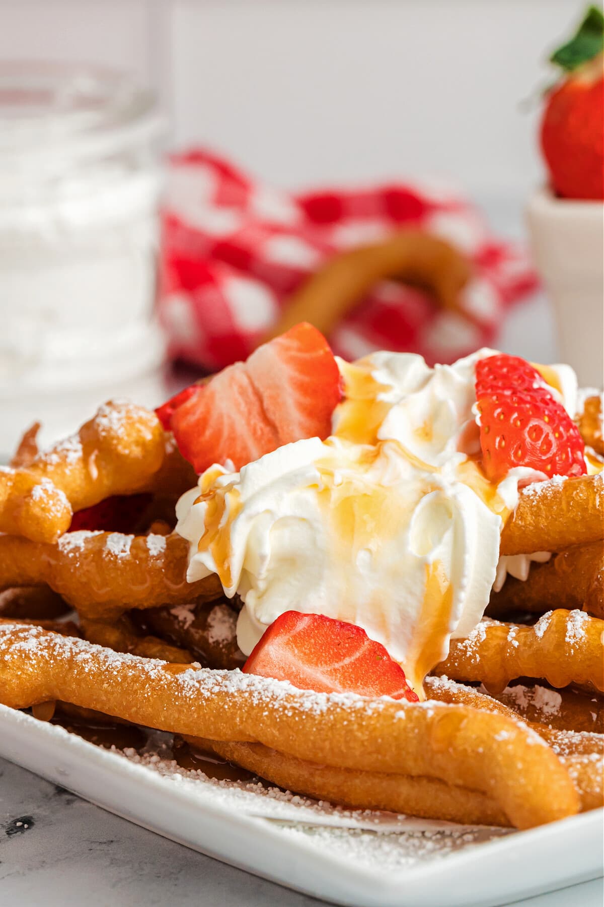 funnel cake fries on white plate with whip cream and strawberries