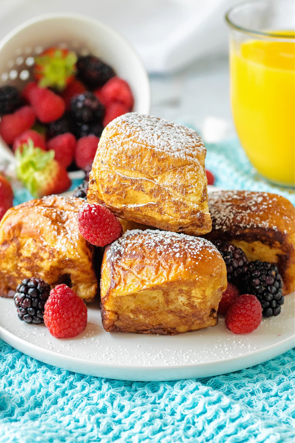 hawaiian roll french toast on white plate with powdered sugar, fruit and orange juice in glass