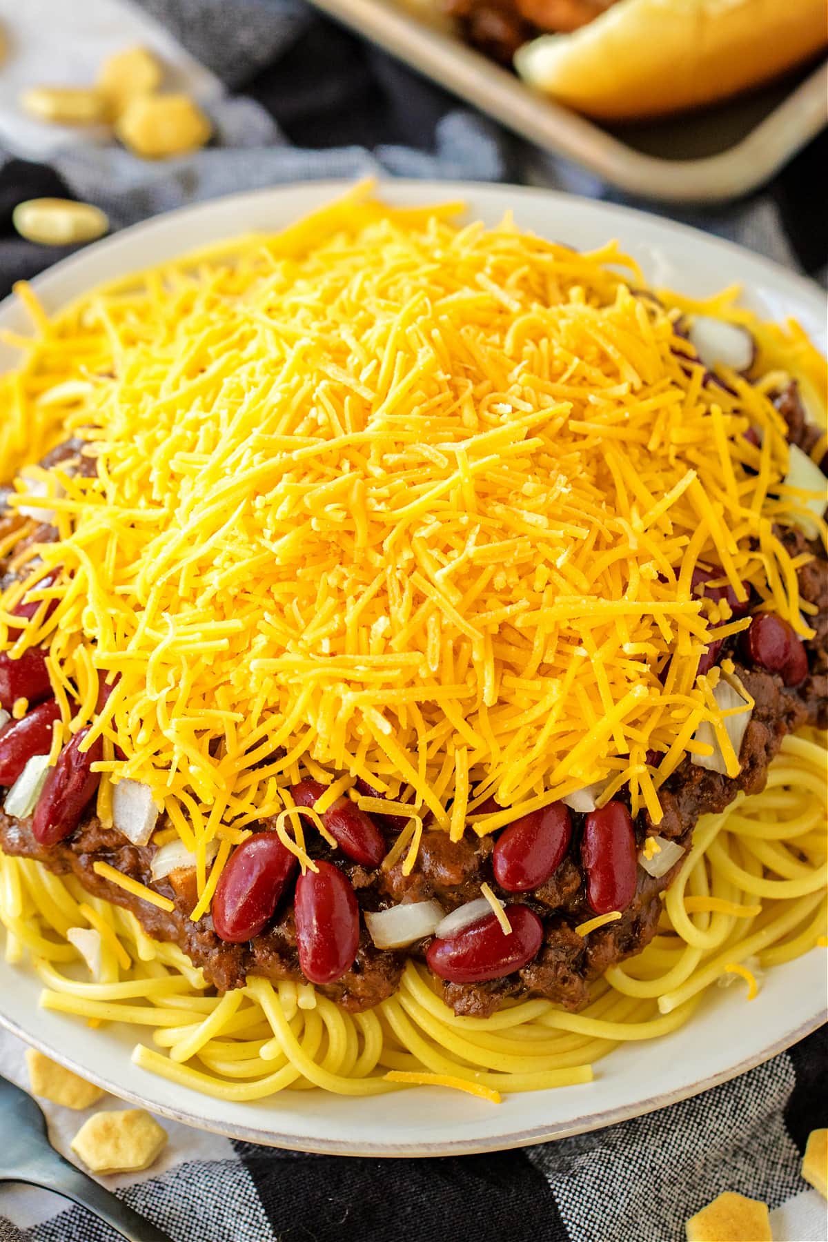 chili on top of cooked spaghetti with beans, onions and cheese on white plate
