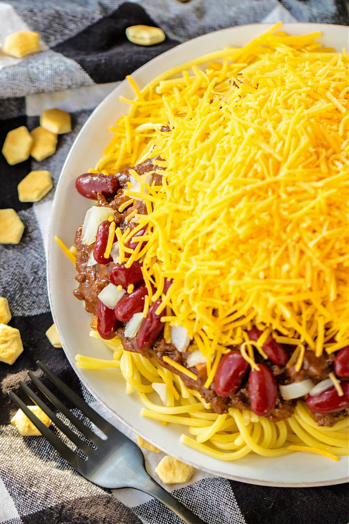 chili with spaghetti, beans, onions and cheese on a white plate