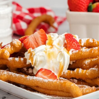 funnel cake fries on white plate with whip cream, strawberries and powdered sugar