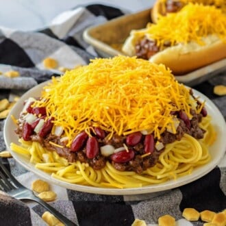 chili on top of spaghetti noodles with beans, onions and cheese on white plate