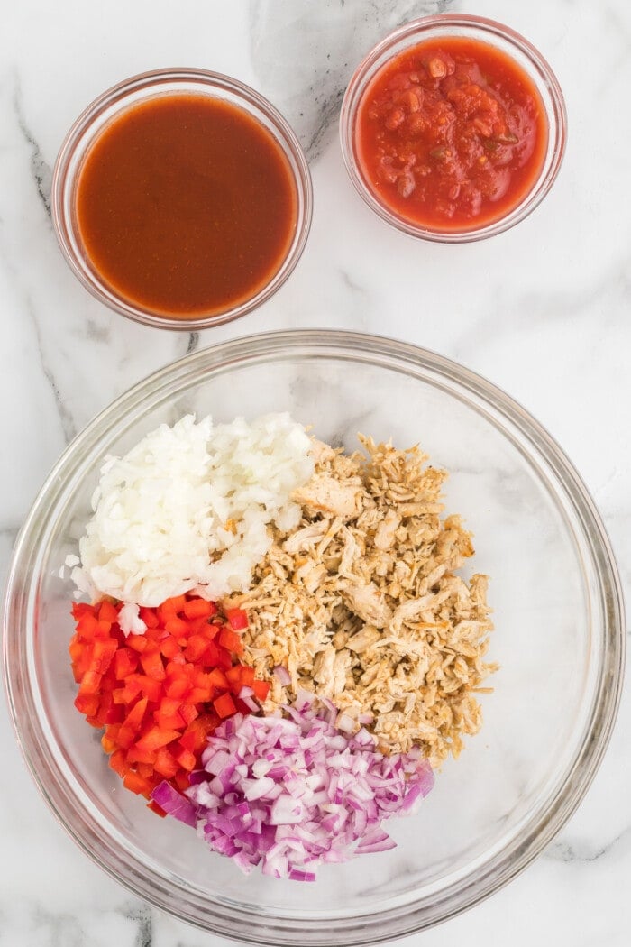 Shredded chicken, onion, and red bell pepper in a glass bowl
