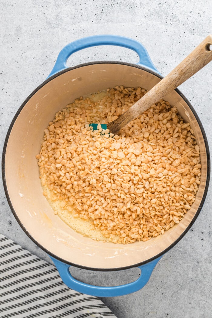 A spatula stirring rice krispie cereal into melted marshmallows
