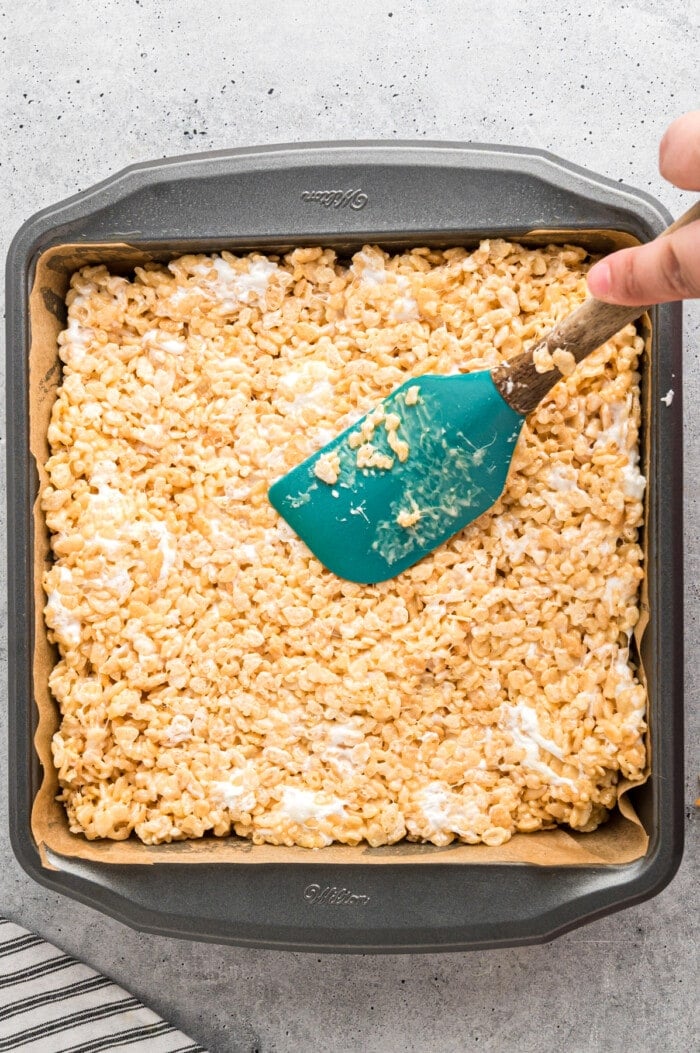 A spatula spreading a homemade Rice Krispie treat mixture into a square pan