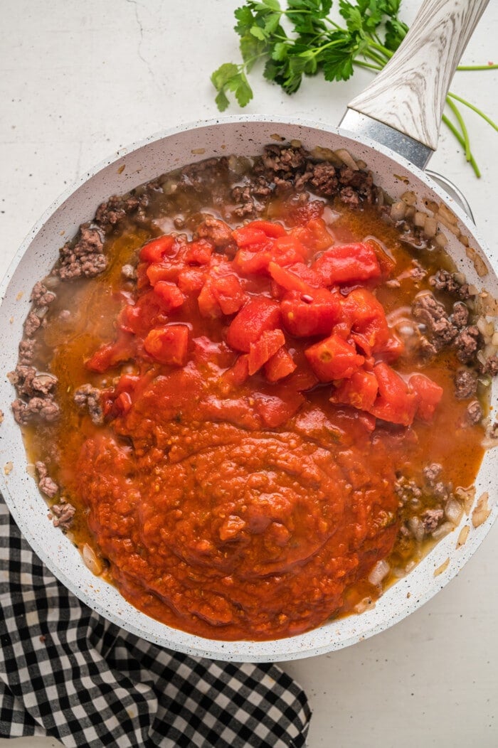 Ground beef, tomato sauce, and canned tomatoes in a skillet