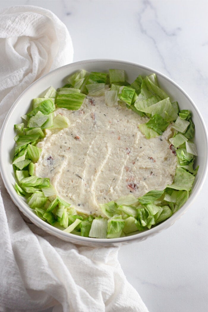 cream cheese mixture in the bottom of a bowl topped with lettuce.
