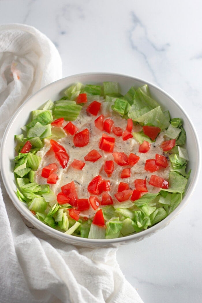 cream cheese mixture in the bottom of a bowl topped with lettuce and chopped tomatoes