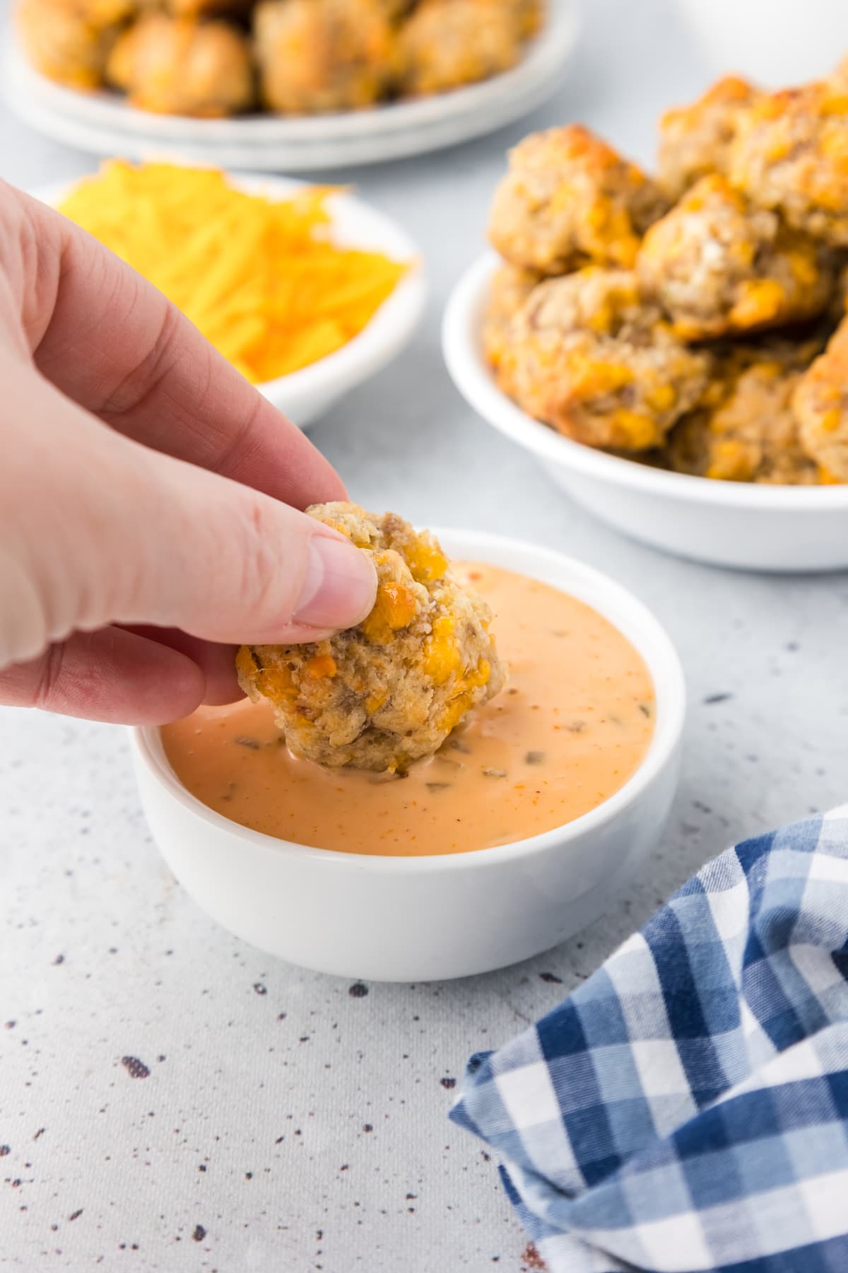 hand dipping cheddar bay sausage ball into cheese sauce