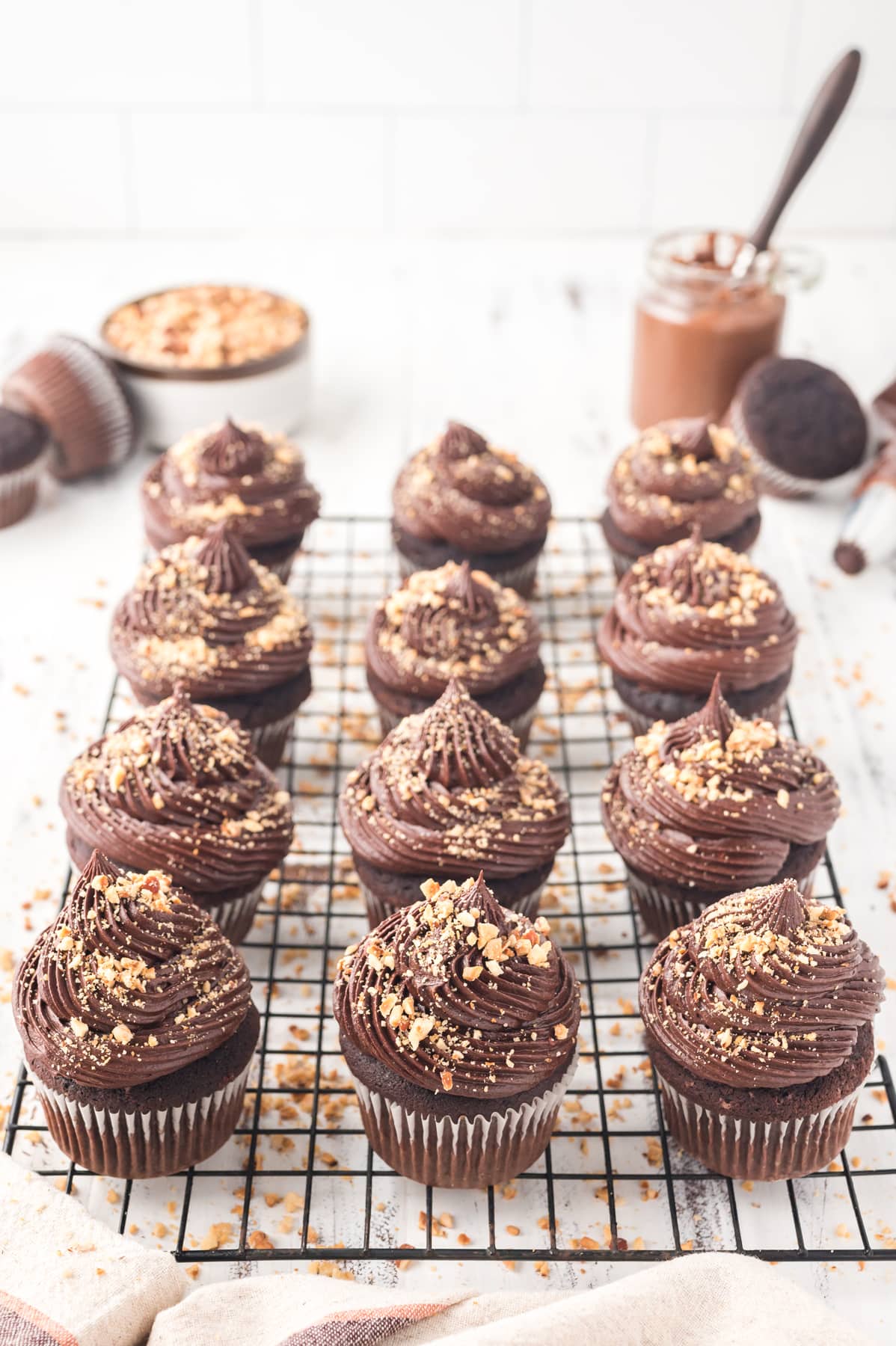 chocolate cupcakes with chocolate frosting and chopped nuts on top on wire rack