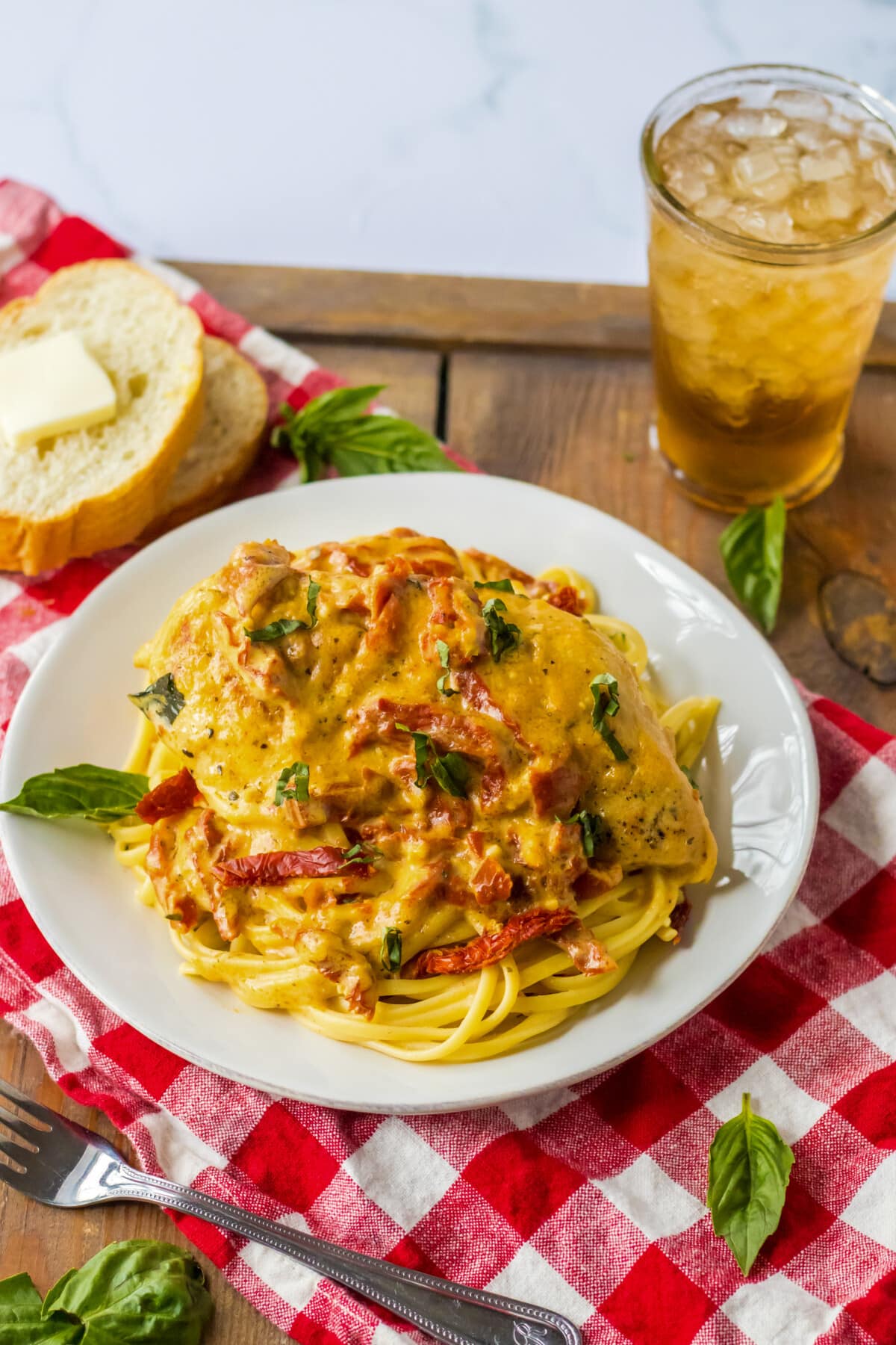crockpot marry me chicken served over pasta with a glass of tea and bread with butter