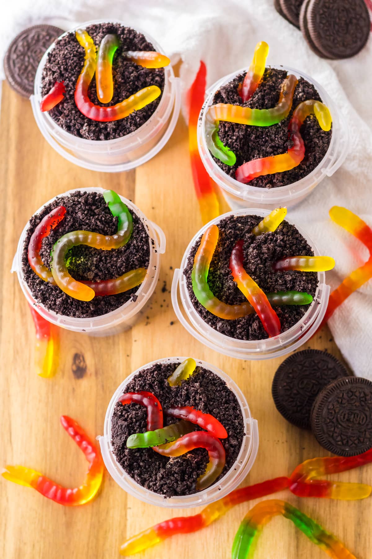 gummy worms on top of chocolate cookie crumbs and dirt pudding in plastic buckets