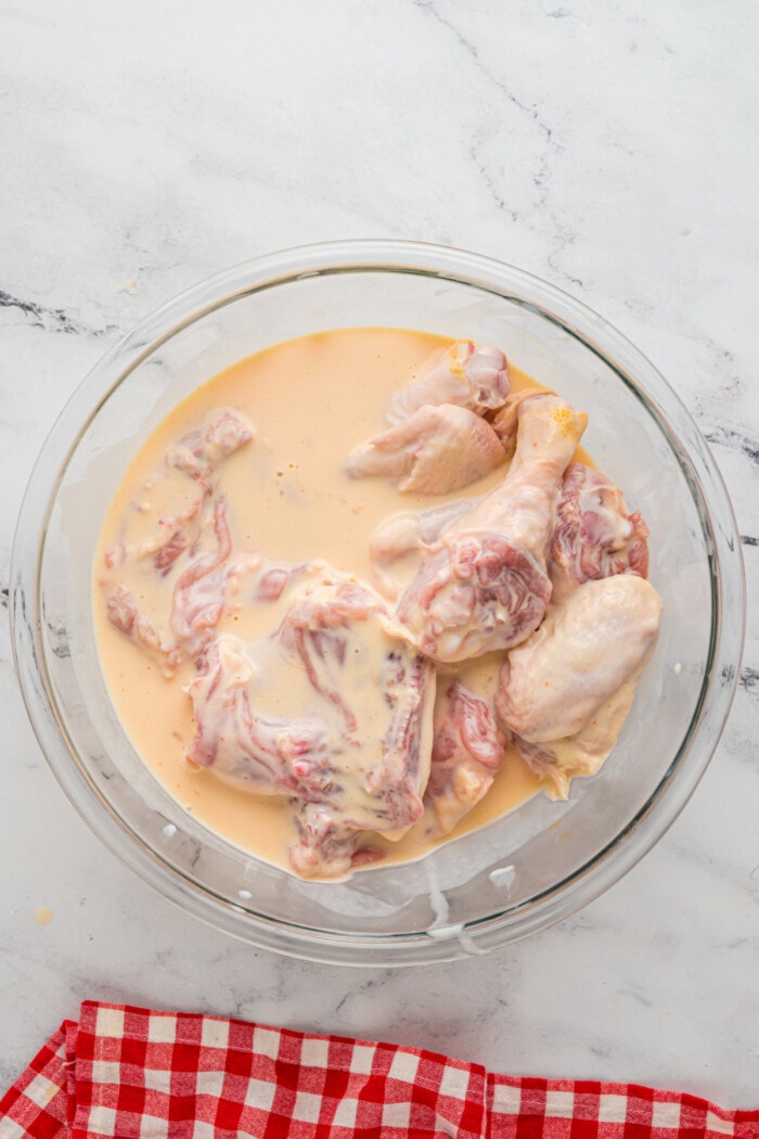 chicken in buttermilk, hot sauce and egg mixture in clear glass bowl
