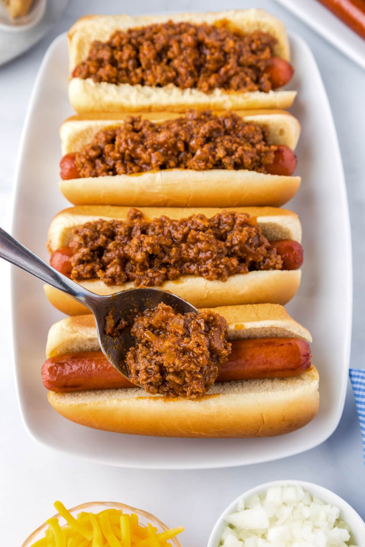spoonful of hot dog chili added to hot dogs in buns