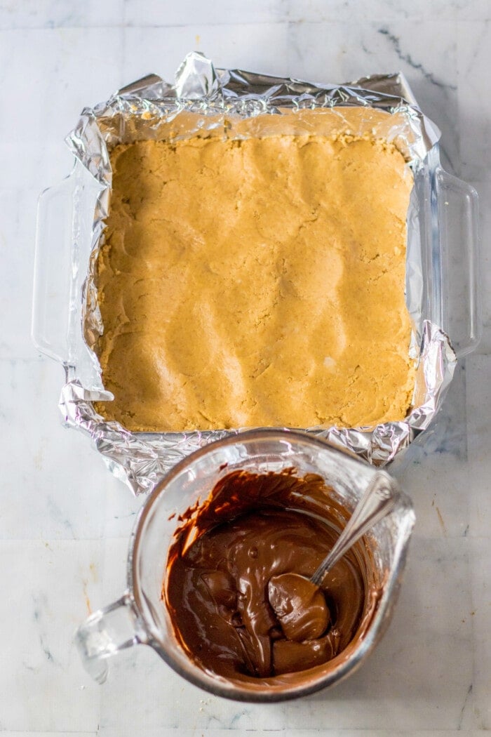 peanut butter bars in square glass baking dish and chocolate frosting in mixing bowl