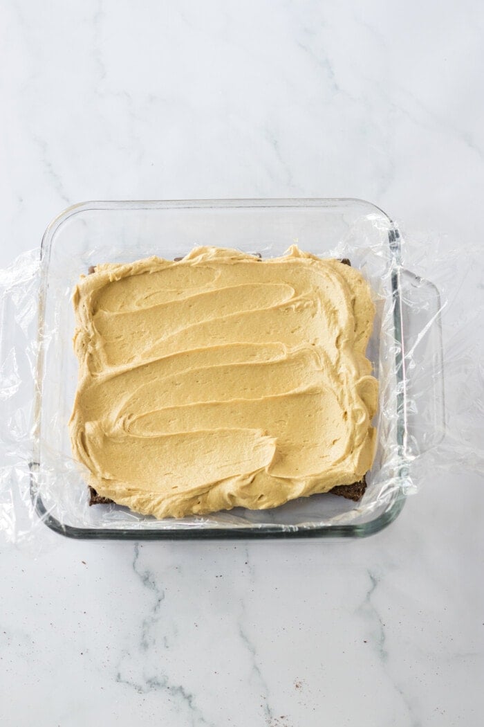 peanut butter on top of chocolate graham crackers in square glass dish