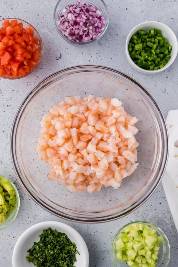 shrimp chopped in glass bowl with other ingredients in small bowls