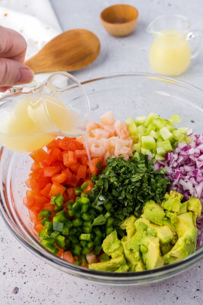 lime juice poured over chopped shrimp and veggies ingredients in glass bowl