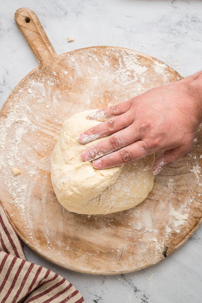 A hand kneading biscuit dough on a cutting board